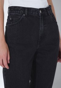 Svarta denimjeans med hög midja, fem fickor och subtila sömdetaljer. Materialet har en strukturerad yta.