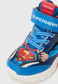 Blaue, von Superhelden inspirierte High-Top-Sneakers mit bedrucktem Design, strukturierten Materialien, Klettverschluss und kontrastierenden Schnürsenkeln. Geox-Branding sichtbar.