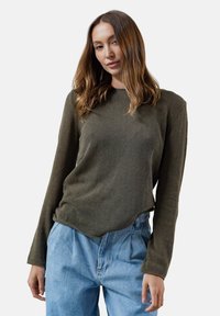 Olive green top z długim rękawem o prążkowanej fakturze z zaokrąglonym dołem. Stylizowany z jasnoniebieskimi dżinsami o wysokim stanie, charakteryzującymi się luźnym krojem.