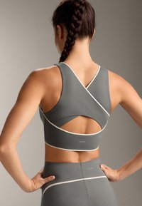 Szary stanik sportowy z krzyżowym tyłem, białymi akcentami oraz wycięciem z tyłu; zestawiony z pasującymi szarymi legginsami.