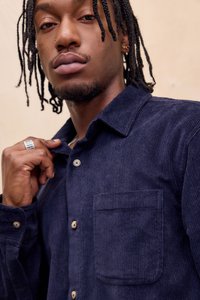 Marineblå kordfløjls skjorte med knappet slidse, messingknapper og en brystlomme. Stoffet har en vertikal ribbet struktur.