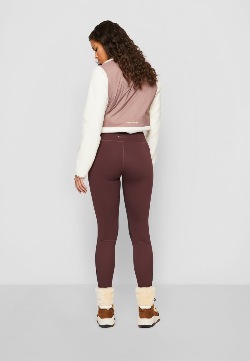 Gekürzte Jacke in Mauve und Creme, mit flauschiger Textur an den Ärmeln, kombiniert mit kastanienbraunen Leggings und braunen Stiefeln mit cremefarbenen Fellakzenten.