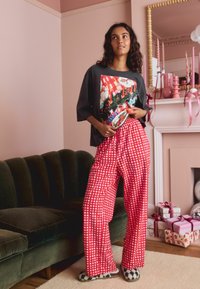 Graphic t-shirt with a festive design and red checkered pajama pants. Black-and-white checkered slippers. Soft textures in a cozy setting.