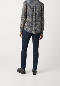 Camicia a maniche lunghe con stampa floreale su base blu navy e punti beige, abbinata a pantaloni slim-fit blu navy e scarpe nere, vista da dietro.