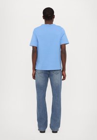 Blå bomull T-skjorte med rund hals og korte ermer, sammen med lyseblå vide jeans med baklommer og en falmet tekstur.