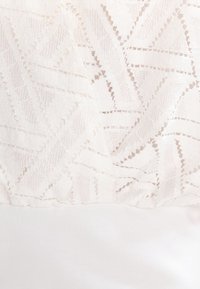 Valkoinen kangas, jossa on geometrinen pitsikuvio, jossa on kolmioita ja timanttimaisia muotoja kiinteän valkoisen materiaalin päällä.