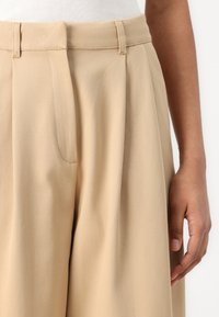 Beiga skräddarsydda byxor med veck, med slät front och bälteshällor. Slät tyg med en subtil glans, utformade för en avslappnad passform.