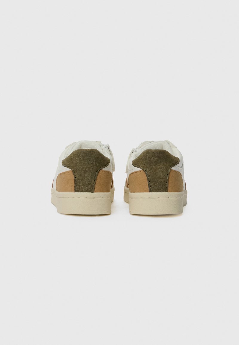 Un paio di sneaker bianche e beige con linguette verde oliva sul tallone, viste da dietro, su uno sfondo bianco semplice.