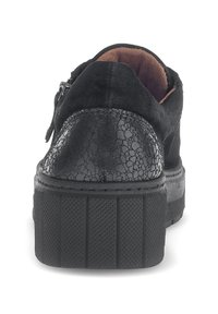 Schwarzer Sneaker mit einer strukturierten, rissigen Lederpartie hinten, Wildleder-Obermaterial und einer dicken, gerillten Gummisohle. Das Innenfutter ist braun und weich.