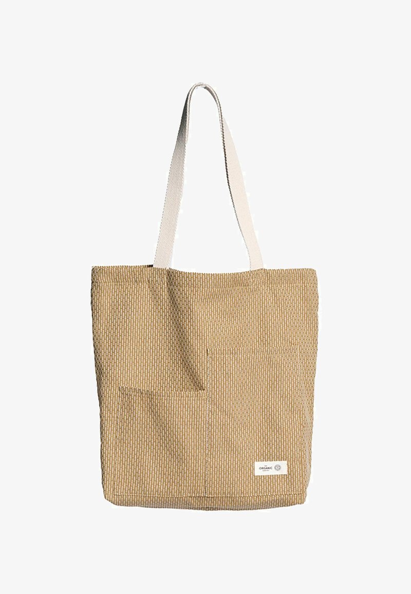 Platnena torba u bež boji s teksturiranim uzorkom; ima dva vanjska džepa i bijelu platnenu naramenicu. Oznaka na donjem desnom dijelu.