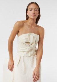 Bezramkowy top z lnu w kolorze kości słoniowej z skręconym przodem i gładką teksturą. Sylwetka jest dopasowana z prostym, eleganckim krojem.