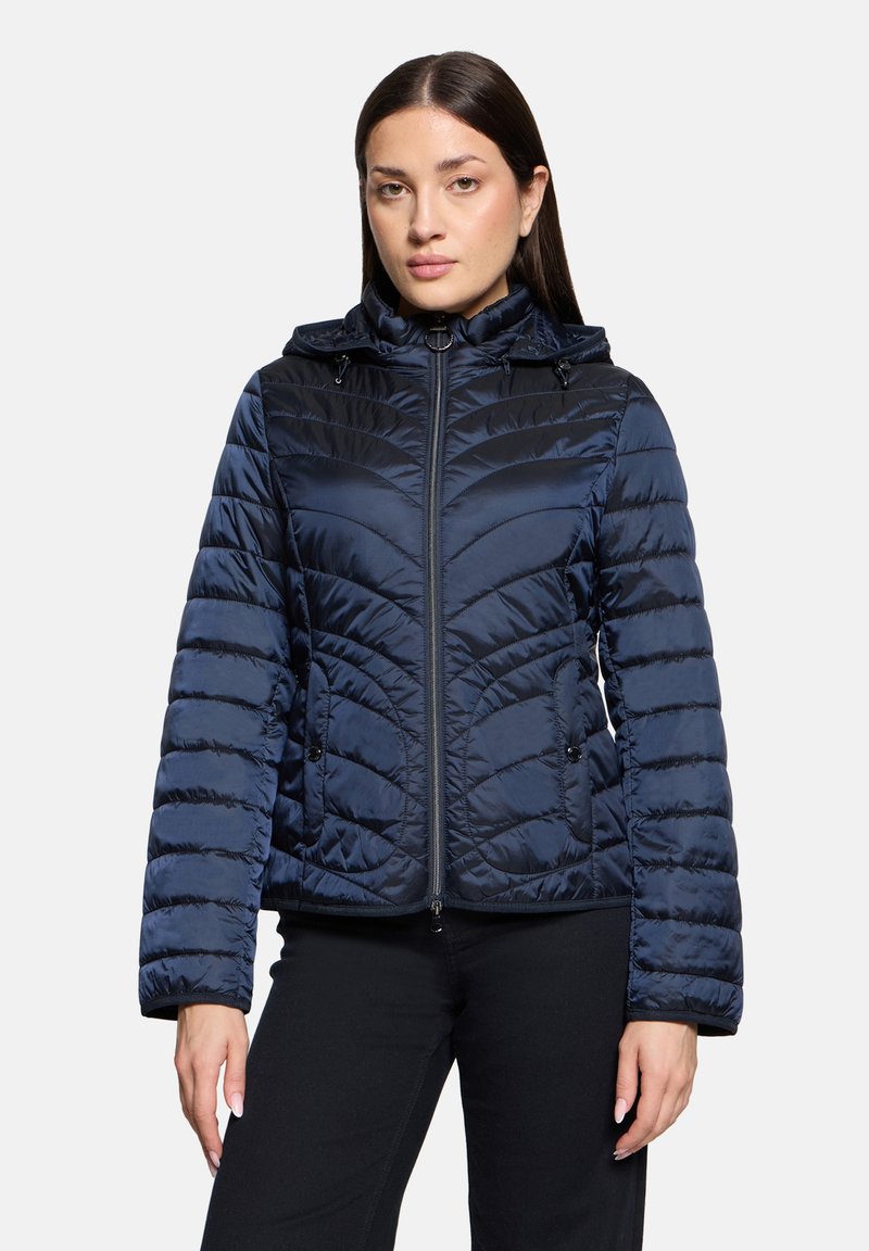 Veste matelassée bleu marine avec fermeture éclair à l'avant, capuche et textures matelassées. Dispose d'une finition lisse et de poignets élastiques pour un meilleur ajustement.