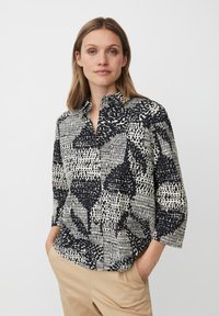 Camicia con colletto in nero e crema con motivi astratti. Presenta maniche lunghe e una vestibilità rilassata. Tessuto morbido con un aspetto texturizzato.