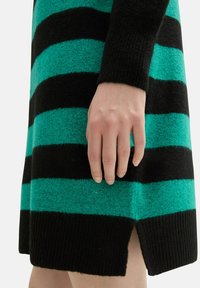 Sukienka dzianinowa w paski charakteryzuje się szerokimi czarnymi i turkusowymi paskami, ribbowanym dołem oraz bocznym rozcięciem. Tkanina ma miękki, teksturowany wygląd.