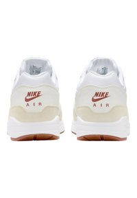 Nike Air-sneakers med vit läder och beige mocka-accenter, med en vit mellansula och en gummigummiyttersula. Röd logotyp på hälen.