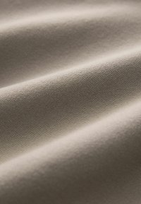Beige tekstil med en glat, let struktureret overflade, der har subtile rynker og folder, hvilket er indicativt for stofdrapering.