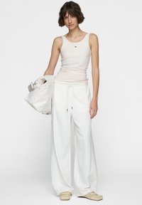 Top sin mangas blanco acanalado con un pequeño logo, combinado con joggers blancos holgados y zapatillas color crema. La modelo sostiene un bolso blanco de estilo despreocupado.