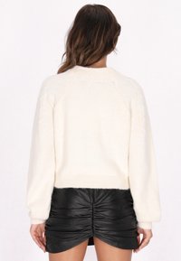 Maglione bianco con una consistenza morbida e pelosa e orlo a costine, caratterizzato da una vestibilità rilassata e maniche raglan, abbinato a una gonna di pelle nera arricciata.