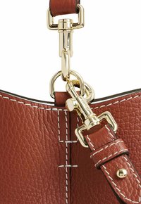 Detalle de un bolso de cuero marrón con herrajes dorados, costuras acentuadas y una correa desmontable con hebilla y cierre.