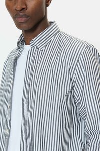 Moški, ki nosi črno-belo srajco s pokončnimi črtami, gumbe zategnjeno, čez preprosto belo majico, prikazano od ovratnika do zgornjega dela trupa.