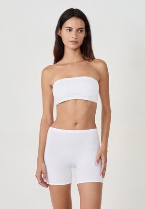 Biały, bawełniany top bez ramiączek w połączeniu z białymi, bawełnianymi szortami. Oba elementy mają gładką teksturę i elastyczne pasy, zaprojektowane z myślą o komforcie i dopasowaniu.