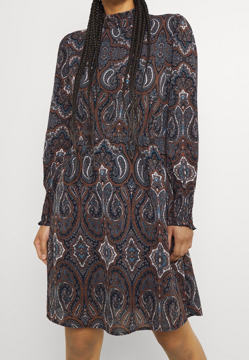 Musta mekko, jossa on paisley-kuvio ruskeassa, sinisessä ja valkoisessa. Pitkät hihat, joissa on kootut hihansuut sekä korkea kaulus; väljät linjat.