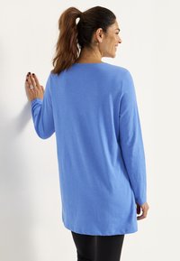 Pitkähiha, vaaleansininen tunika, joka on rento ja valmistettu pehmeästä materiaalista. Kyllä pyöreä kaula-aukko ja hieman kaareva helma, yhdistettynä mustiin legginsseihin.