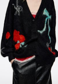Czarny kardigan z kwiatowym haftem w kolorach czerwonym, morskim i białym. Miękka faktura, z głębokim dekoltem w serek i pojedynczym zapięciem na guzik.