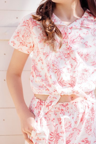 Rosa Bluse mit Blumenmuster und kurzen Ärmeln, versehen mit einem geknoteten Band an der Taille, kombiniert mit passender Shorts mit einem elastischen Bund.