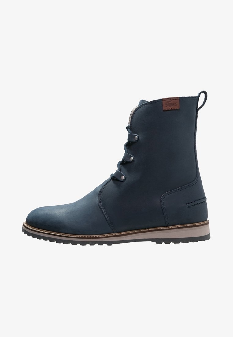 Bottine en cuir bleu marine avec trois œillets métalliques, semelle marron contrastante et patch logo marron près du haut à l'arrière.