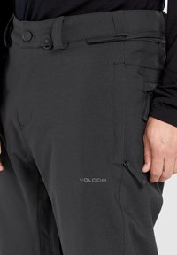 Pantalons de snowboard noirs au design ajusté, fabriqués en matériau durable. Comprend une poche zippée et un logo sur la cuisse.