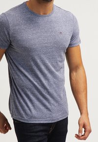 Šedé melírované tričko slim fit s kulatým výstřihem. Obsahuje malé vyšívané logo na prsou a krátké rukávy.