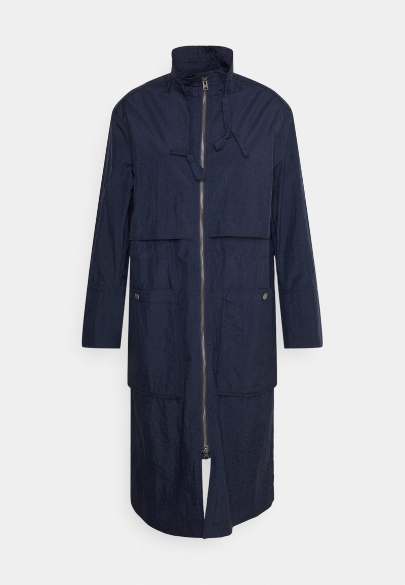 Marineblauwe lange jas van textuurmateriaal, met een hoge kraag, een ritssluiting aan de voorkant, twee opgestikte zakken en een recht model.