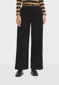 Black corduroy wide-leg pants with a textured surface and a high waist, paired with a leopard print belt. Footwear is dark loafers.