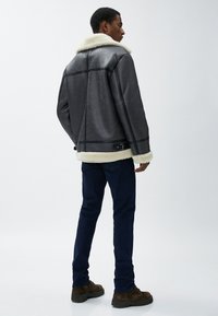 Herre grå shearling-foderet jakke med krave, der har en glat tekstur, sort syning og justerbare side spændebånd, parret med mørke jeans.