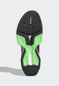 Semelle en caoutchouc noire de chaussure de sport avec accents en caoutchouc vert, surface texturée à motif et logo central pour une meilleure adhérence et durabilité.