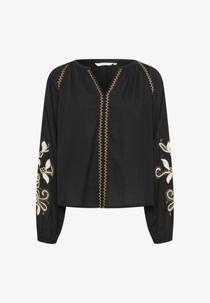 Blouse noire à manches longues avec des motifs floraux blancs brodés sur les manches ; présente un col en V et une couture décorative dorée sur le devant.