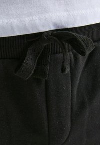 Sorte sweatpants med struktureret stof, med snor i taljen og synlige sømdetaljer under en hvid skjorte.