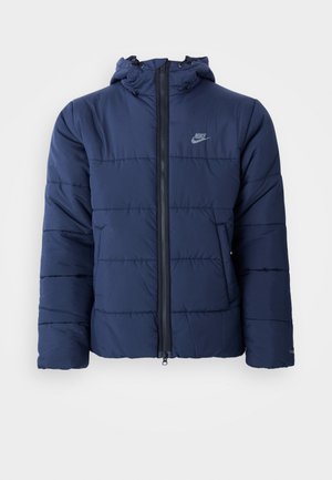 Doudoune bleu marine avec capuche, dotée d'une fermeture éclair à l'avant, d'un motif de couture horizontal et d'un petit logo sur le haut à gauche de la poitrine.