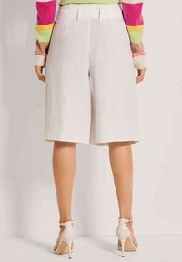 Witte linnen culottes met een brede pootontwerp, voorzien van een op maat gemaakte tailleband en zijzakken, gecombineerd met hoge hakken sandalen.