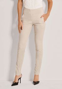 Beige hoge taillebroek met een aansluitend ontwerp, zijzakken en een gladde textuur, gecombineerd met zwarte puntenhakken.