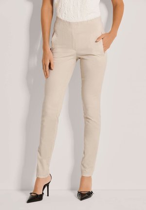 Beige hoge taillebroek met een aansluitend ontwerp, zijzakken en een gladde textuur, gecombineerd met zwarte puntenhakken.