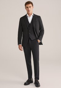 Melnā uzvalkā ar pieguļošu žaketi un biksēm, kas kārtota virs balta krekla. Izskats papildina atbilstoša veste un pulētas melnas kurpes.