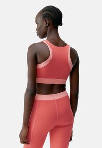 Korall színű sportmelltartó és leggings szett, sima anyaggal, hátsó kivágással és ellentétes pasztell díszítéssel. A varrás nélküli kivitel kényelmet nyújt.