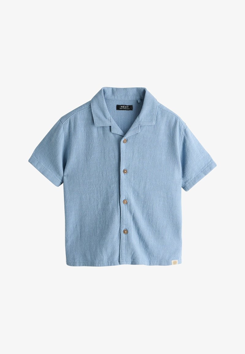 Chemise bleu clair à manches courtes boutonnée, en tissu texturé, boutons en bois et petite étiquette blanche en bas de l'ourlet.