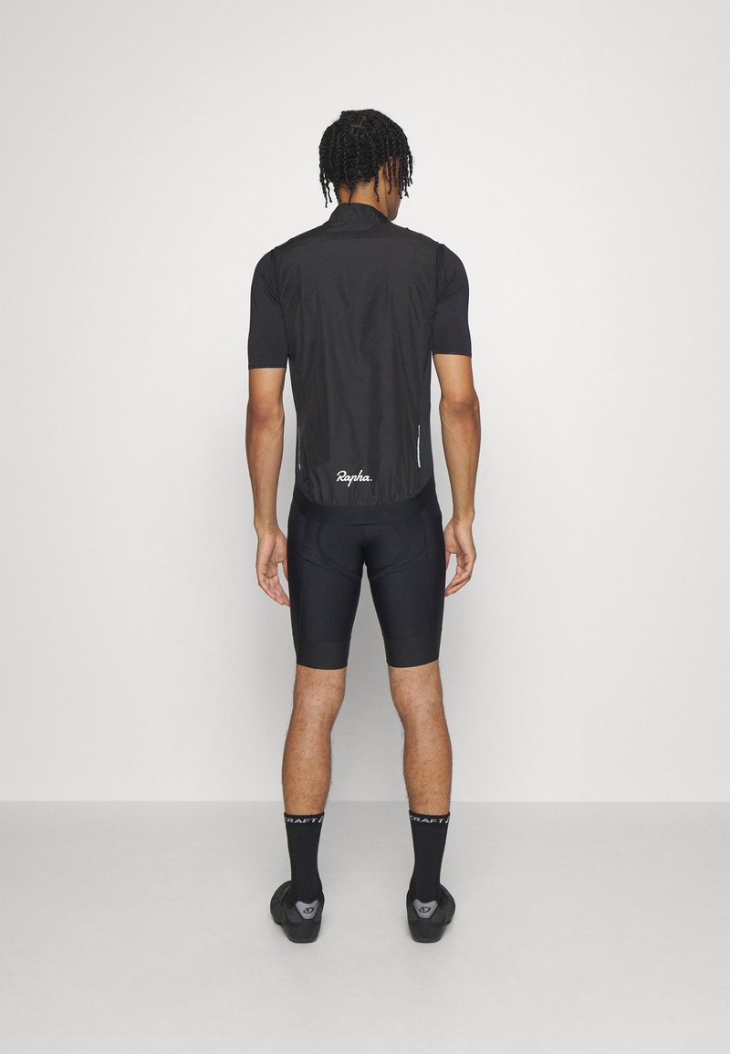 Gilet de cyclisme noir avec un col haut, coupe ajustée et matériau léger. Comprend deux poches latérales et un logo à l'arrière. Shorts et chaussettes noirs.