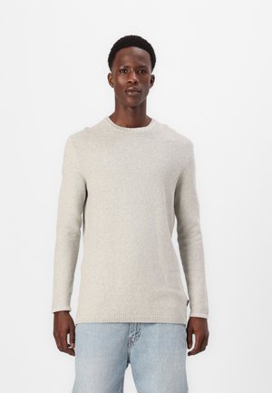 Ljust grå stickad tröja med långa ärmar, rund hals, strukturerat mönster och ribbad fåll, bärs med ljusblå jeans.