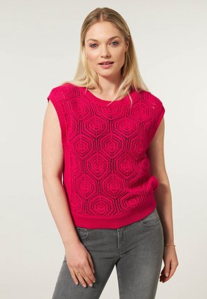 Korte mouwen, gebreide top in helder roze, met een hexagonaal patroon, geribbelde onderkant en een ontspannen pasvorm. Gecombineerd met grijze jeans.