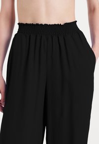 Pantaloni neri con vita arricciata, caratterizzati da una texture liscia e tasche laterali, progettati per il comfort e la facilità nei movimenti.