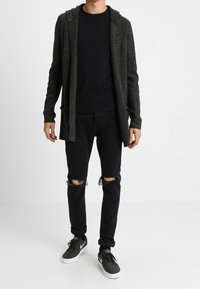 Grå stickad cardigan med huva, svart t-shirt, rivna svarta jeans och grå sneakers med vita sulor. Enkel design och avslappnad passform.